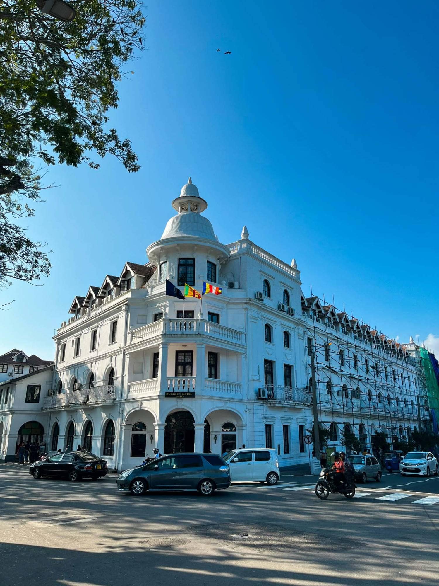 A white colonial hotel building with a domed corner tower, on a busy Kandy street