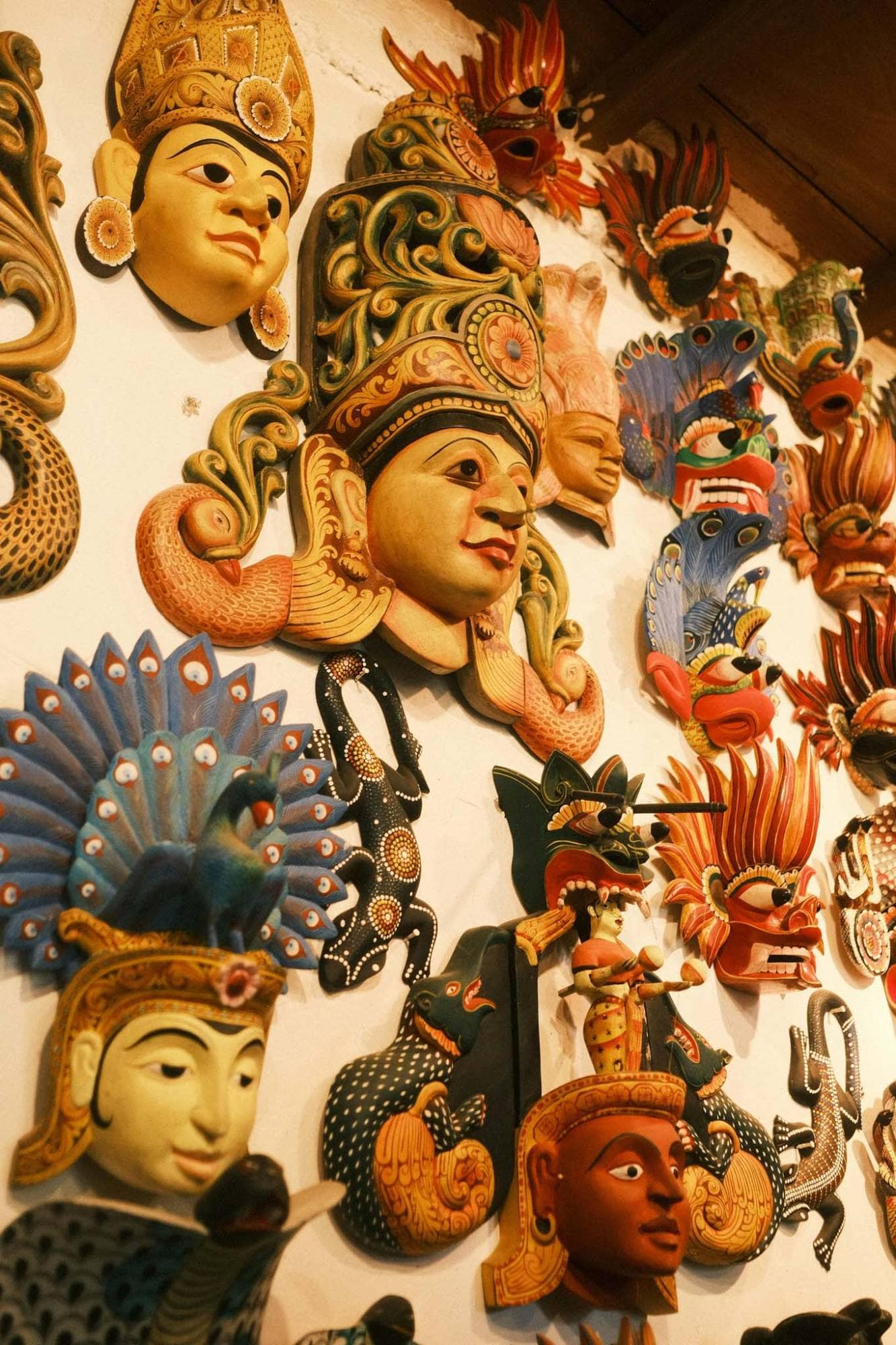 A wall of brightly painted masks and carvings, including peacock and cobra headdresses