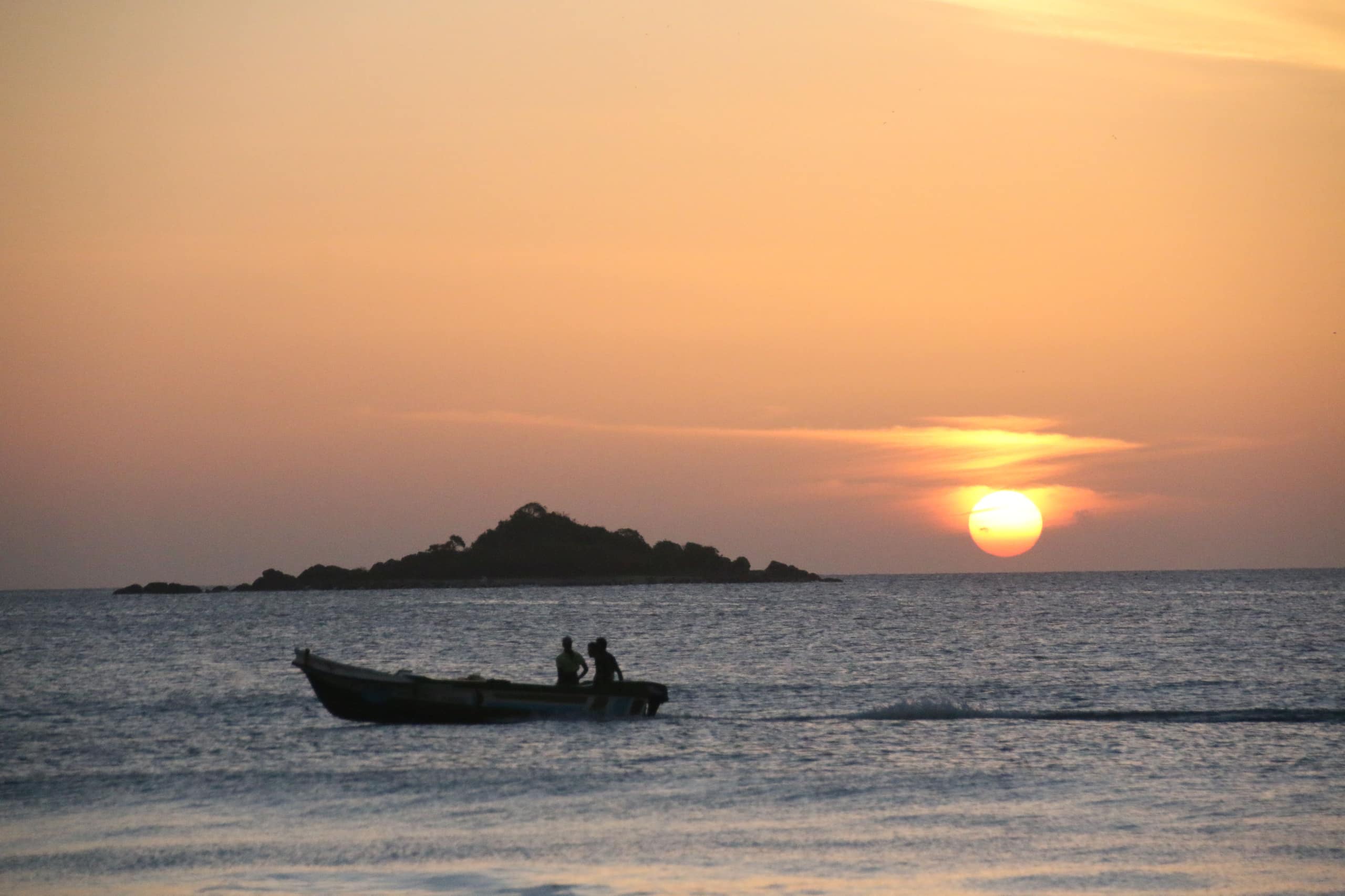 The sun low over a still tank, a bare tree in the foreground and a stupa on the far shore